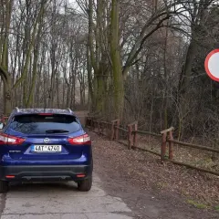 Niebieski Nissan na leśnej drodze, obok znak zakazu ruchu. Kierowca ryzykował wjazd pod zakaz ruchu, mandat murowany.
