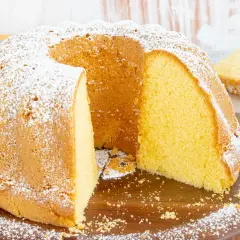 Ein saftiger vanille kuchen, bestäubt mit Puderzucker, wartet darauf, angeschnitten zu werden. Ein Stück ist bereits auf einem Teller angerichtet.
