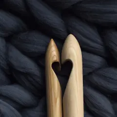 Dwa drewniane szydełka tworzą serce na tle grubiutkiej, ciemnoszarej wełny merino. Co to jest wełna merino? To miękkie włókno idealne do dziergania.