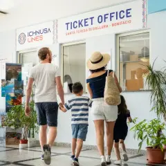 Famiglia in coda all'ufficio biglietti per la Corsica con bambini. L'avventura inizia qui!