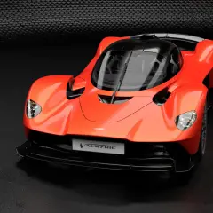 Pomarańczowy Aston Martin Valkyrie, supersamochód o futurystycznym designie, prezentuje swoje aerodynamiczne linie na ciemnym tle.