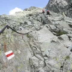 Łańcuchy i czerwono-białe oznaczenia szlaków na skalistym zboczu, wskazujące na jedne z najtrudniejszych szlaków w Tatrach.