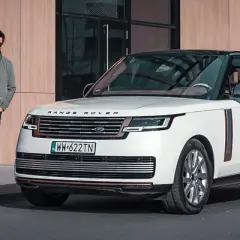 Elegancki mężczyzna w okularach stoi obok białego Range Rover 2025 z czarnym dachem.