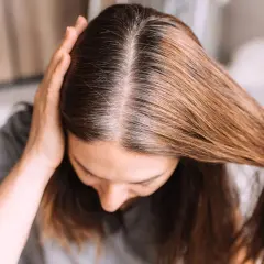 Una mujer se toca el cabello, mostrando mechones grises que explican porque salen canas.