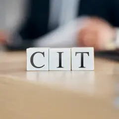 Trzy białe kostki z literami C, I, T ułożone na drewnianym blacie. Temat: podatek CIT.