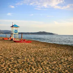 Torre di salvataggio e barche rosse sulla sabbia dorata, con il mare calmo e le colline sullo sfondo. Paestum mare.