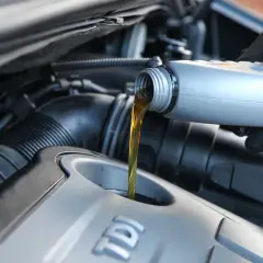 Händer med handskar häller olja i en bilmotor. Valet mellan 5w30 vs 5w40 beror på din bil.