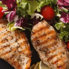 Due petti di pollo grigliati, conditi con erbe aromatiche, serviti con un'insalata fresca, pomodorini e spicchi di limone.