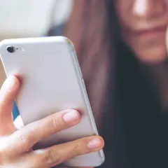 Kobieta trzyma telefon, zastanawiając się, jak wysłać mms.