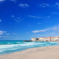 Spiaggia di Palermo con mare turchese e case bianche con tetti rossi.
