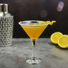 Elegancki koktajl Sidecar w kieliszku z cukrowym rantem, obok cytryny i shakera.