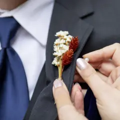 Dłoń przypina do marynarki delikatną brustaszę z suszonych kwiatów.