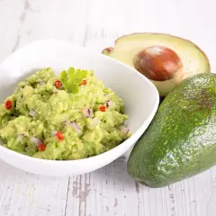 Jak zrobić guacamole z awokado: świeże awokado, miska z pysznym guacamole z cebulą i papryczką chili, ozdobione natką pietruszki.