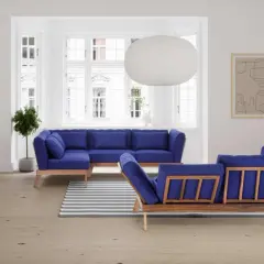 Ein tiefblaues Sofa mitten im Raum, mit Holzrahmen und passenden Kissen. Ein Streifen-Teppich liegt davor.