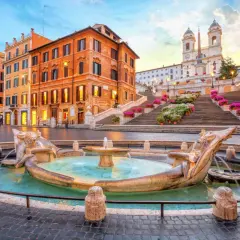 Fontana della Barcaccia e scalinata di Trinità dei Monti a Roma, con edifici storici e fiori colorati.