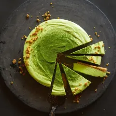 Ein köstliches Matcha-Dessert, in Stücke geschnitten, mit zerbröselten Keksen und feinem Matcha-Pulver bestreut.