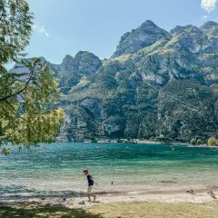Chłopiec bawi się na plaży nad Jeziorem Garda, w tle góry. Idealne pola kempingowe czekają na odkrycie.