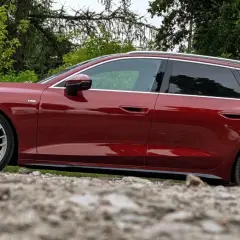 Lśniące, czerwone Audi A6 C9 Avant stoi na kamienistym podłożu, otoczone zielenią.