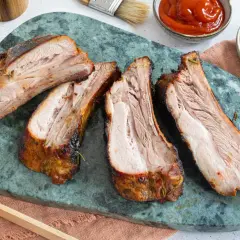 Saftige, dicke Rippe vom Grill, perfekt gegart und auf einem grünen Marmorbrett angerichtet. Dazu passen Ketchup und Senf.