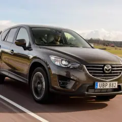 Brun Mazda CX-5 kör på en landsväg i Sverige. Föraren verkar ha ett problem med bilen.