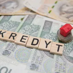Kredyt 400 tys jaka rata? Mały czerwony domek na stosie monet i banknotów symbolizuje marzenie o własnym M.
