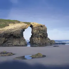 Arco natural en la costa de Ribadeo, con el mar y el cielo azul de fondo.