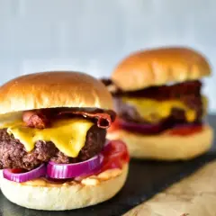Zwei saftige Burger mit geschmolzenem Käse, knusprigem Speck und roten Zwiebelringen. Die Burger patties sind perfekt gegrillt.