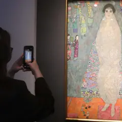Besucherin fotografiert das größte Gemälde der Welt, ein detailreiches Porträt einer Frau in einem opulenten Kleid, umgeben von bunten Figuren.