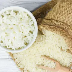 Ciotola di riso bianco cotto accanto a un sacco di riso crudo. Il riso crudo è noto per i suoi rimedi naturali.