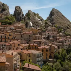 Houses cling to a mountainside in Pietrapertosa, Italy, beneath dramatic rock formations.