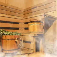 Drewniana sauna z miotełką i kadzią, idealna na zakwasy po treningu. Para unosi się, tworząc relaksującą atmosferę.
