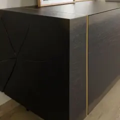 Dunkles Sideboard mit markanter, geometrischer Front. Die Maserung des Holzes und die goldene Leiste unterstreichen, was bedeutet massiv: ein Möbelstück, das Charakter und Beständigkeit ausstrahlt.