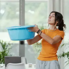 Frau fängt tropfendes Wasser mit blauer Schüssel auf, ein Zeichen für Feuchtigkeit unter Dachpappe.