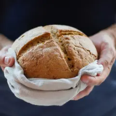 Okrągły bochenek chleba na lnianej ściereczce, trzymany w dłoniach. Zastanawiasz się, który chleb ma najmniej kalorii?