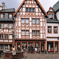 Fachwerkhaus-Idylle in Mainz. Eine Frau sitzt am Brunnen, umgeben von malerischen Gassen – hier sind die echten Mainz Geheimtipps!