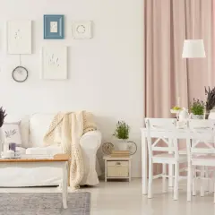 Przytulny salon w stylu shabby chic z białą kanapą, drewnianym stolikiem i pastelowymi dodatkami.