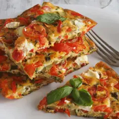 Une part d'omelette aux légumes colorée, garnie de tomates, courgettes et fromage frais, avec une feuille de basilic.