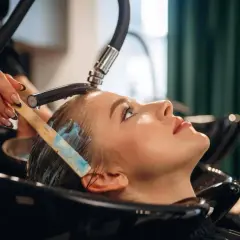 Profesjonalna pielęgnacja włosów farbowanych w salonie. Stylistka aplikuje niebieską maskę na mokre włosy klientki.