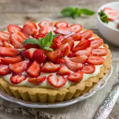 Prosta tarta z truskawkami, udekorowana listkami mięty, wygląda apetycznie na drewnianym blacie.
