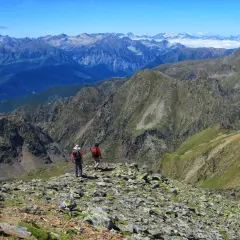 Dos excursionistas exploran las impresionantes **rutas de Esterri d'Àneu**, rodeados de picos montañosos y un cielo azul.