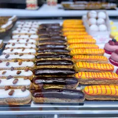 Une alléchante liste pâtisserie française : éclairs au chocolat, à la vanille et au glaçage jaune rayé de rouge, ainsi que des tartelettes aux amandes.