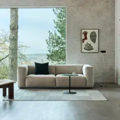 Gemütliches Wohnzimmer mit einem Sofa in millennial grey, einem Holzsessel und einem Bücherregal vor einem Fenster mit Blick ins Grüne.