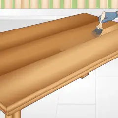 Applying a clear coat to a DIY table. The wooden surface is being brushed with a clear finish, enhancing its natural grain.