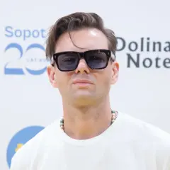 Rubens piosenkarz w okularach przeciwsłonecznych i naszyjniku z koralików, pozuje na tle napisu "Sopot 20 Lat" i "Dolina Noteci".