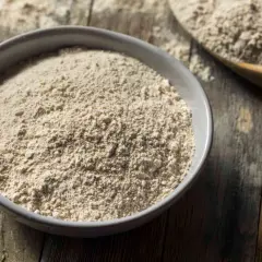 Un bol de farine complète, un équivalent de farine 00 pour des recettes rustiques. Une cuillère en bois en arrière-plan.