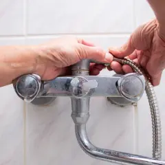 Hands working to fix a shower faucet, detaching the shower hose.