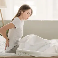 Junge Frau mit Rückenschmerzen im Bett, die eine ungünstige Schlafposition einnimmt, die eine ISG-Blockade verursachen könnte.