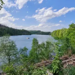 Ein ruhiger See mit einem kleinen Haus am Ufer, umgeben von grünen Wäldern. Der genkeltalsperre rundweg lädt zum Spaziergang ein.