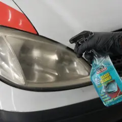 Mano guantata spruzza detergente su un faro opaco. La lucidatura fari quanto dura dipende dal metodo, ma un buon prodotto può fare miracoli.