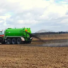 Czerwony traktor z zielonym wozem asenizacyjnym rozprowadza poferment z biogazowni na polu.